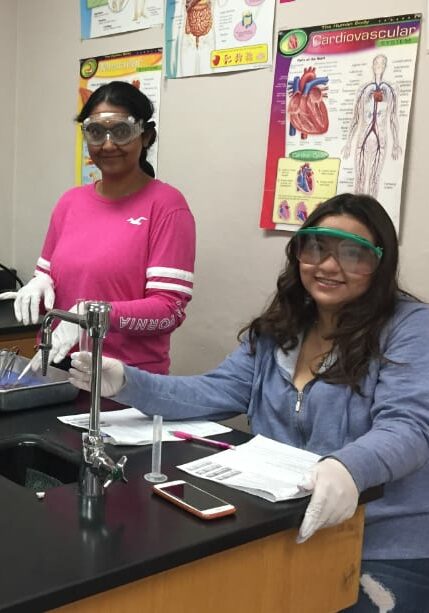 two students wearing chemistry goggles in science class